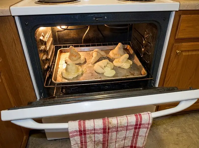 breadsticks partway baked, pale dough, two leaning sideways, one split with pale cheese oozing unbrowned onto the sheet, Parmesan speckle still pale