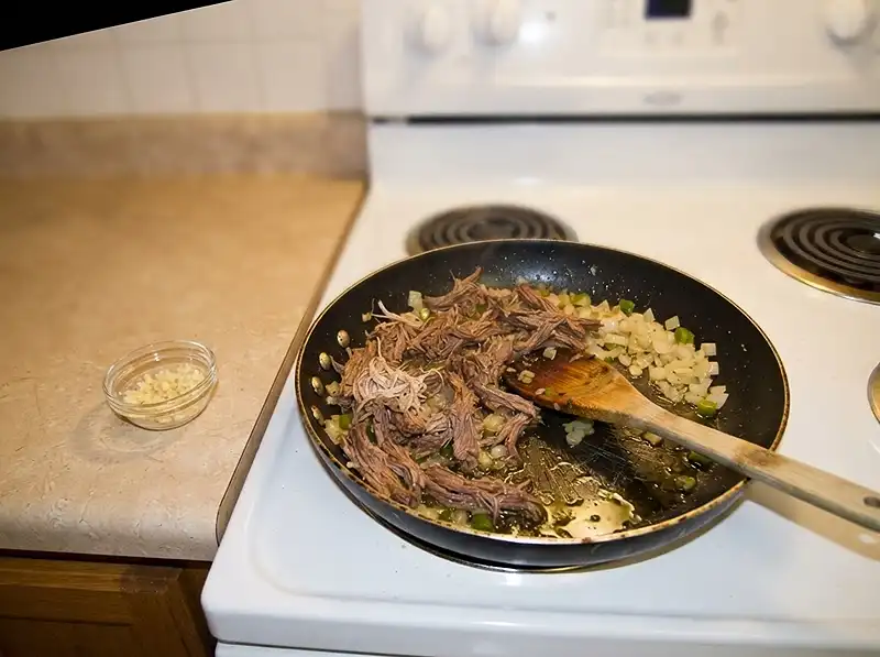 Pabellón Criollo (Venezuelan Shredded Beef) 4 sautéed onion and green pepper softening in the oil with the shredded beef just stirred in, shreds uncoated and some still pale and dry, garlic waiting beside the stove