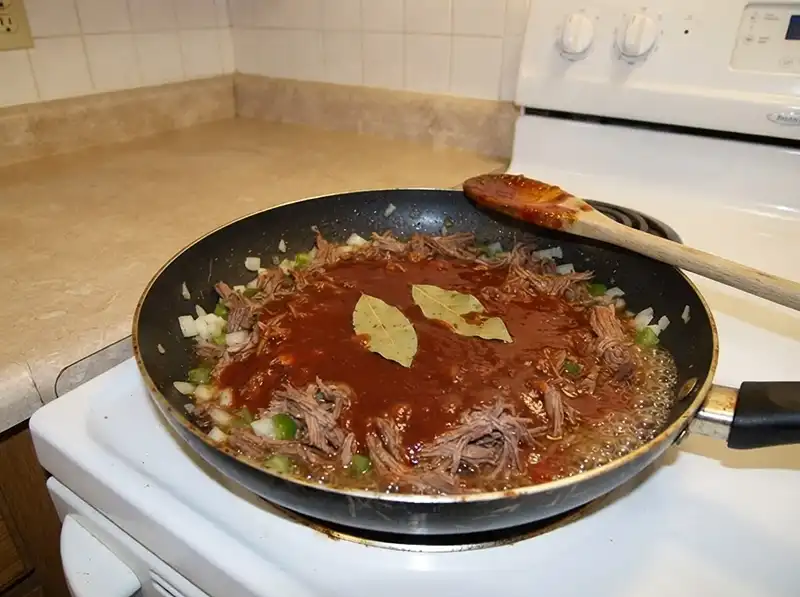 Pabellón Criollo (Venezuelan Shredded Beef) 5 the thick tomato-and-broth mixture just poured over, still a glossy thin liquid layer, two bay leaves floating on top, nothing reduced yet